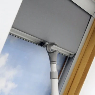 Close-up view of a skylight blind operated with a manual pole, showcasing its easy-to-use design. The sleek grey blind is installed in a natural wood-framed window, providing a practical solution for hard-to-reach windows while offering privacy and light control."